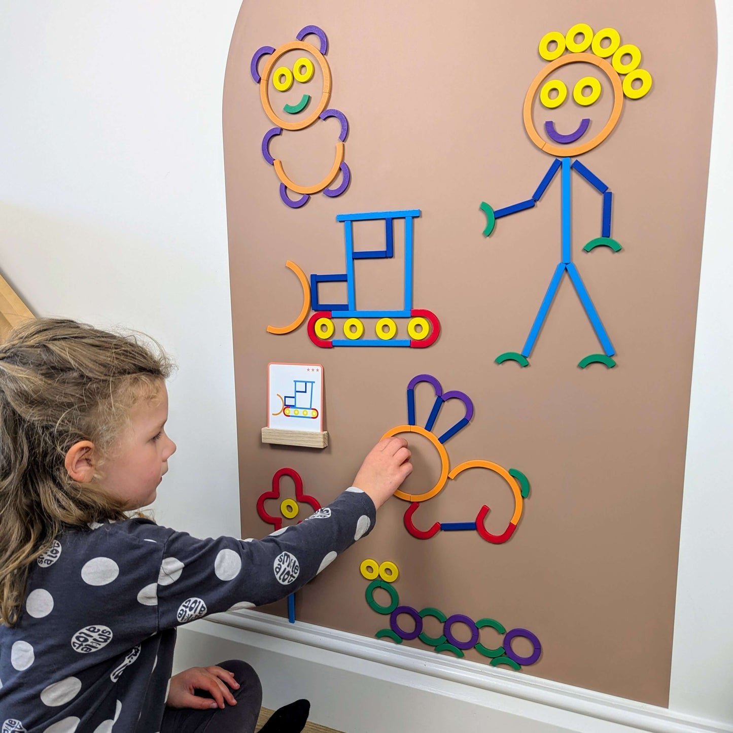 Child playing with a clay coloured wall decal with colourful wooden magnetic shapes