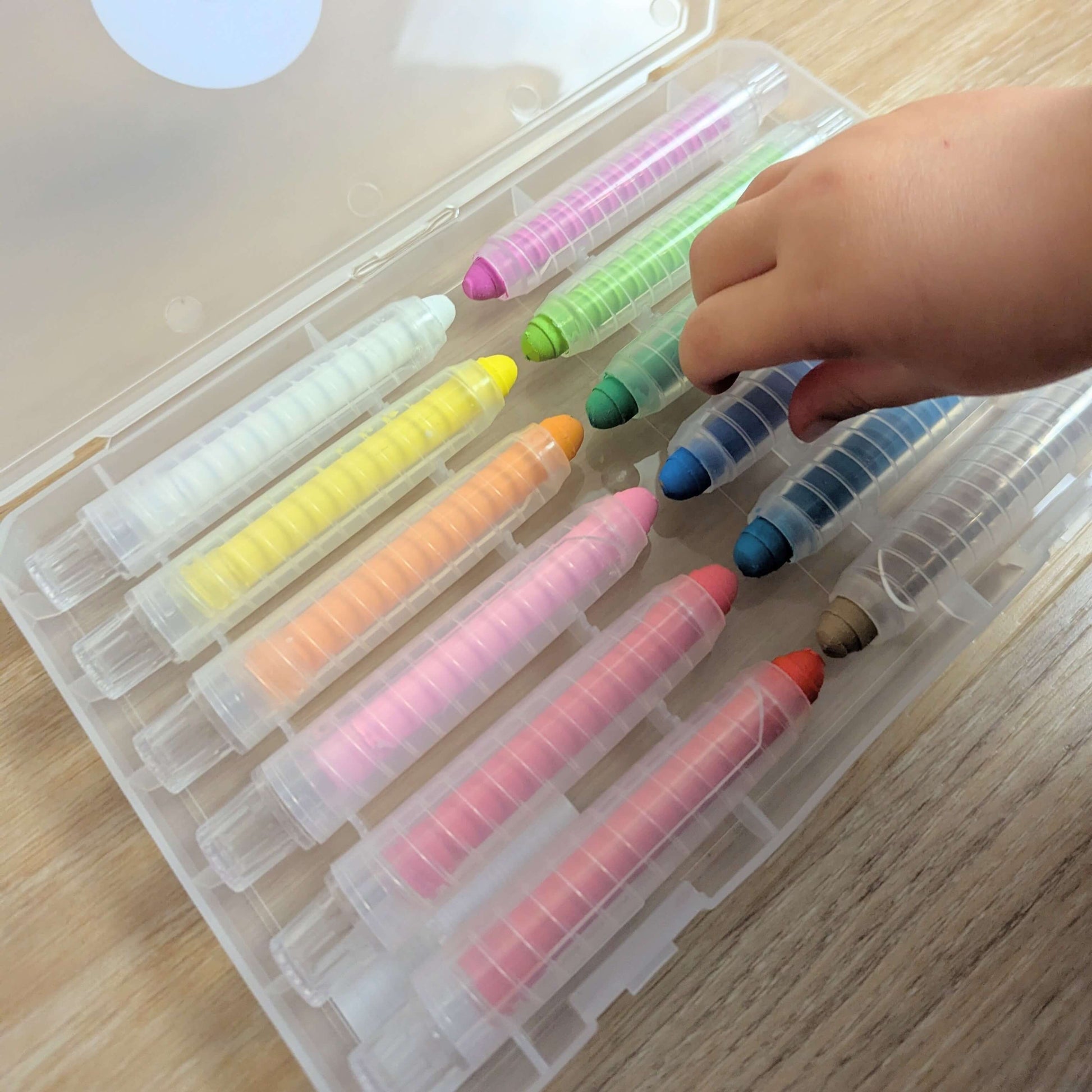 a childs hand picking up a blue crayon out of a case of 12