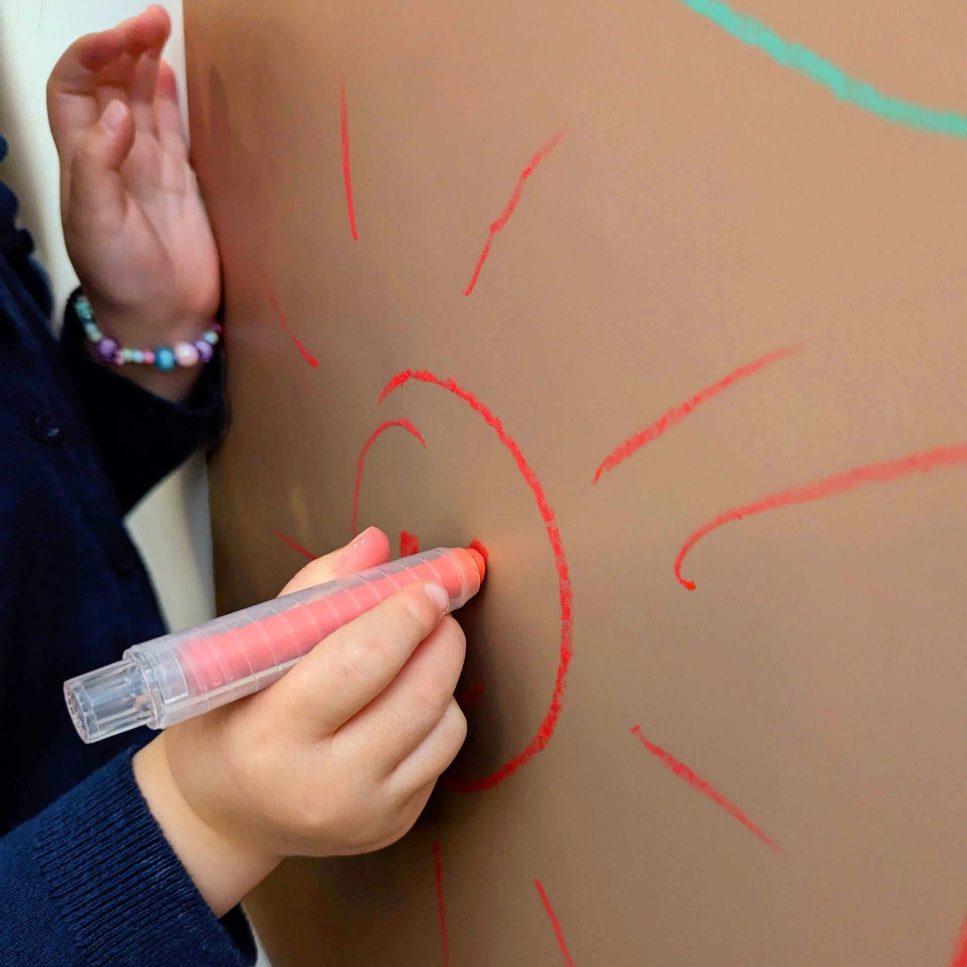 a child drawing with a red crayon on a clay coloured wall surface