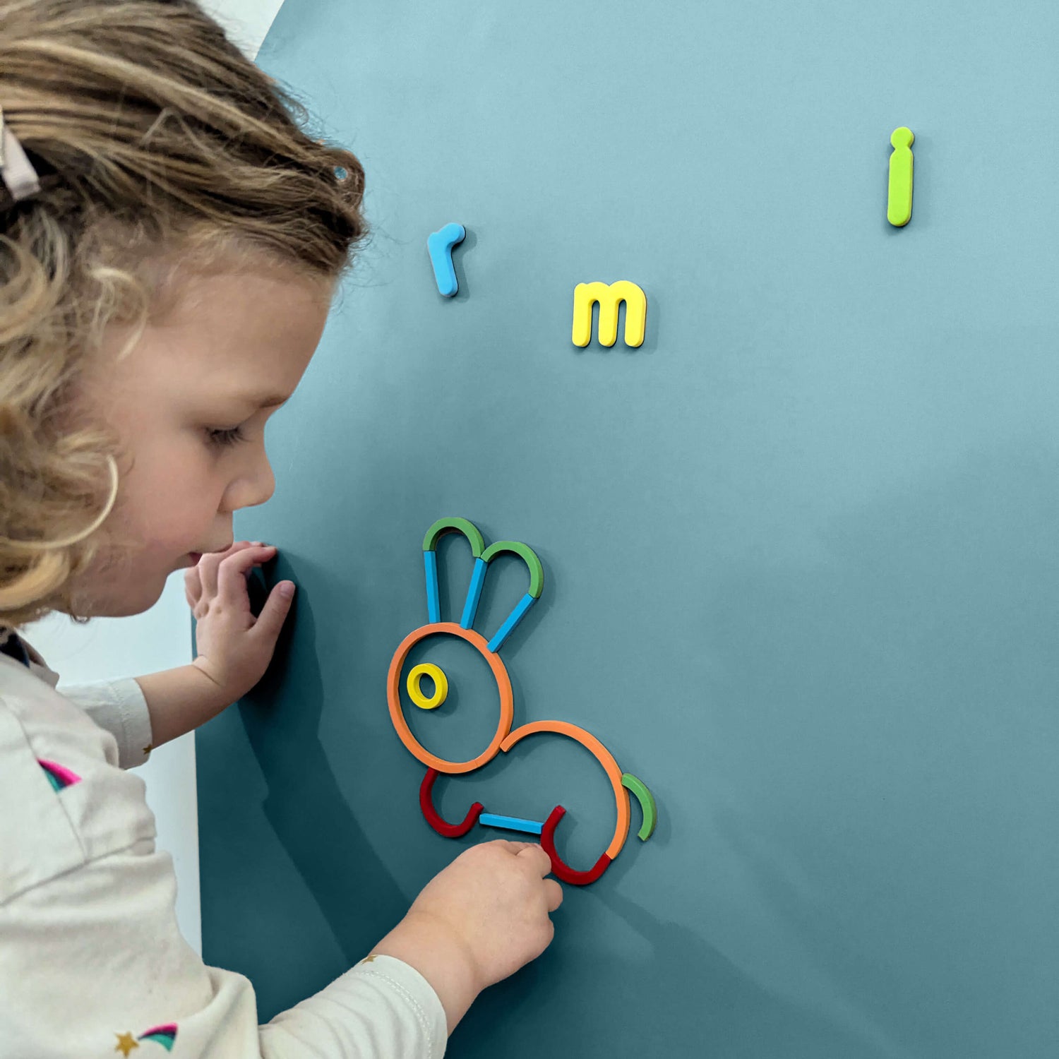 Close up of a young girl playing with colourful magnetic shapes on a teal coloured wall decal