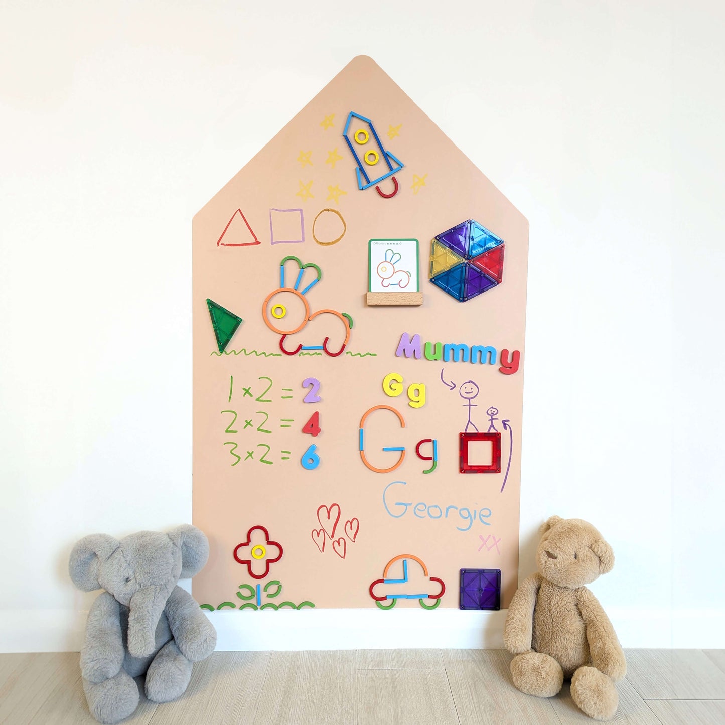 Pink house shaped wall decal covered in witing and magnetic toys and flanked by two cuddly bears