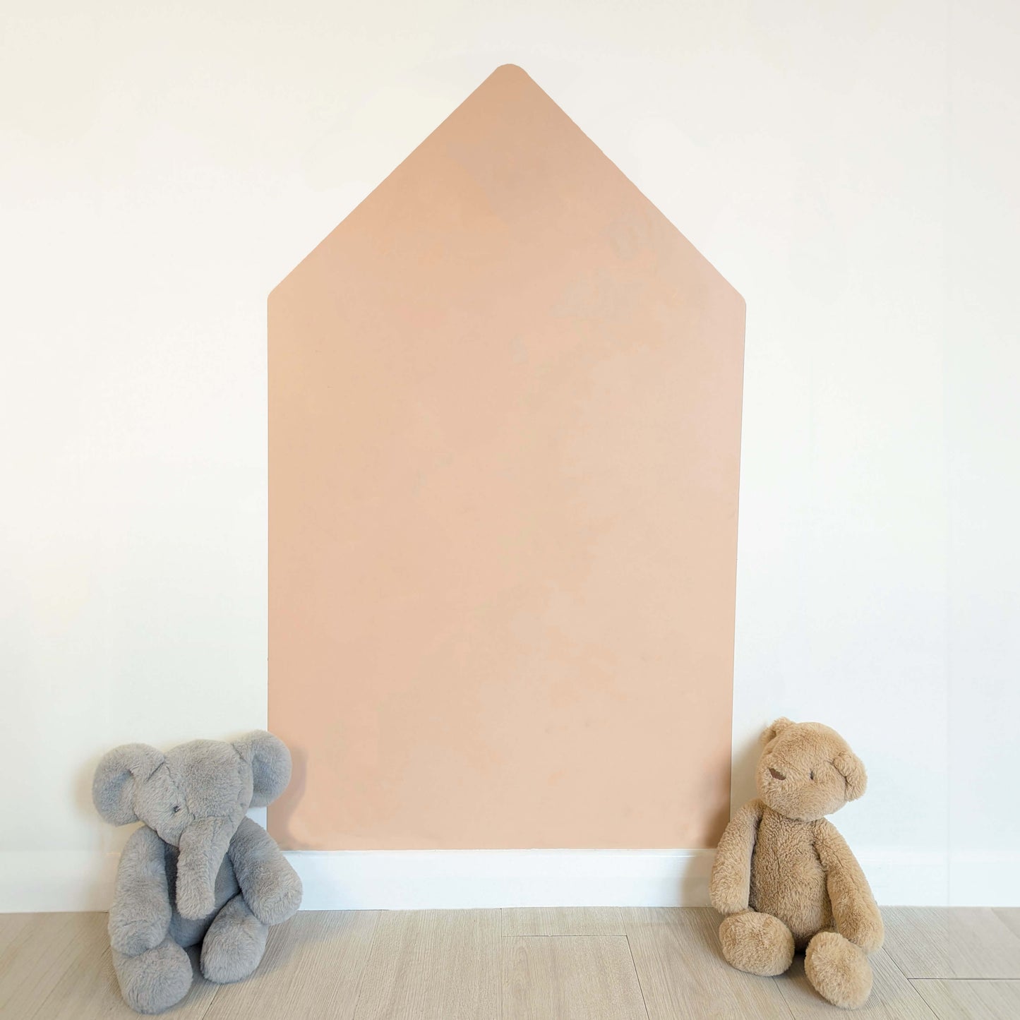 Blank pink house shaped wall decal on a white wall white two teddies sat on grey floor in front of it