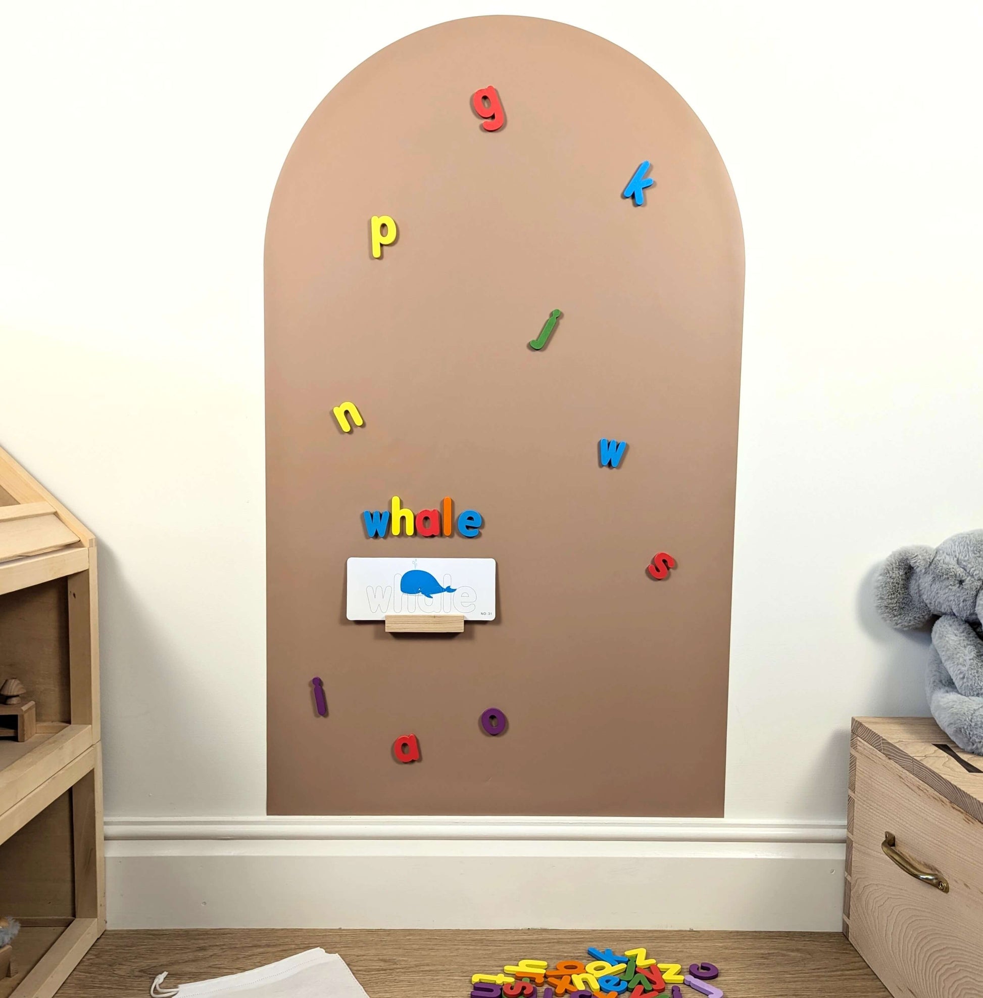 scattered colourful magnetic letters and a card spelling whale on a clay coloured wall decal