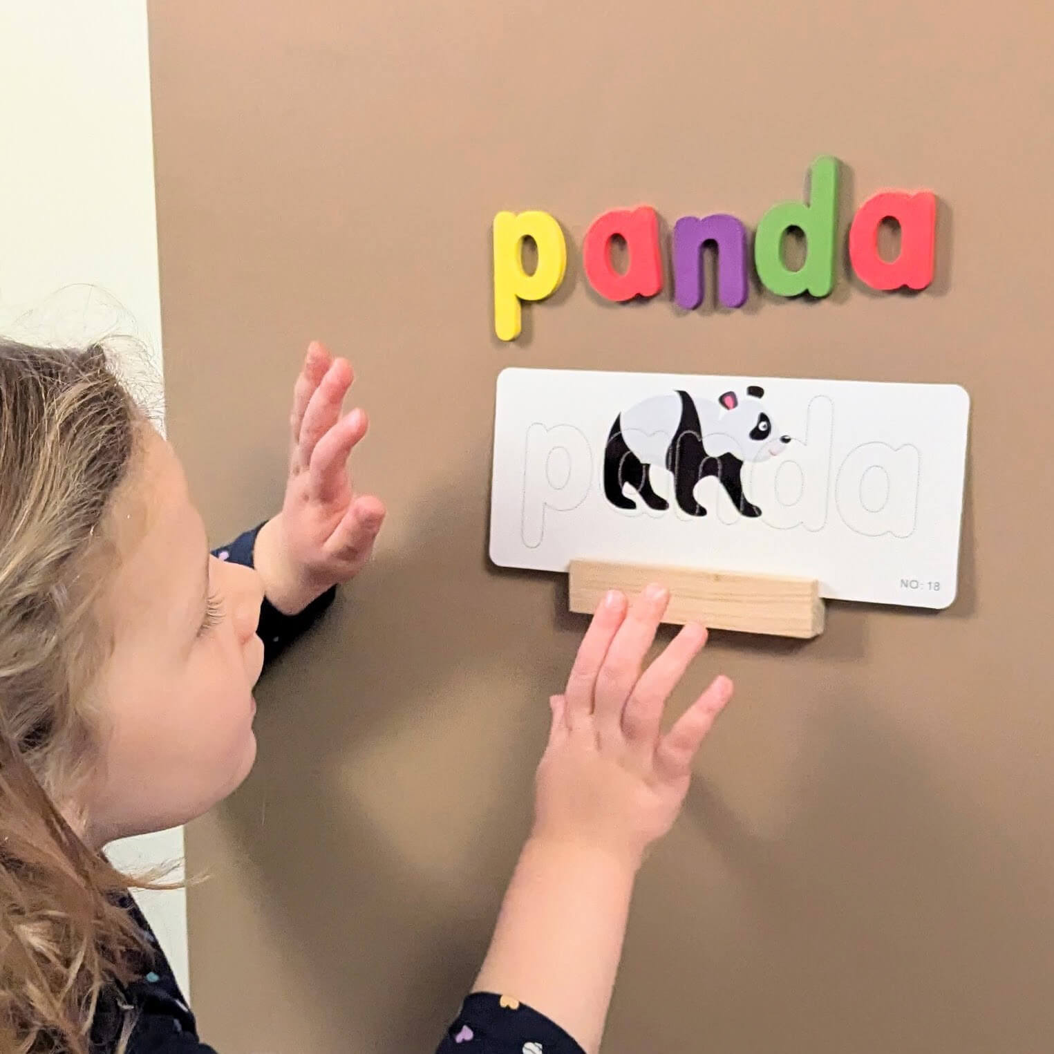 a child spelling the word panda with colourful letters on a brown board