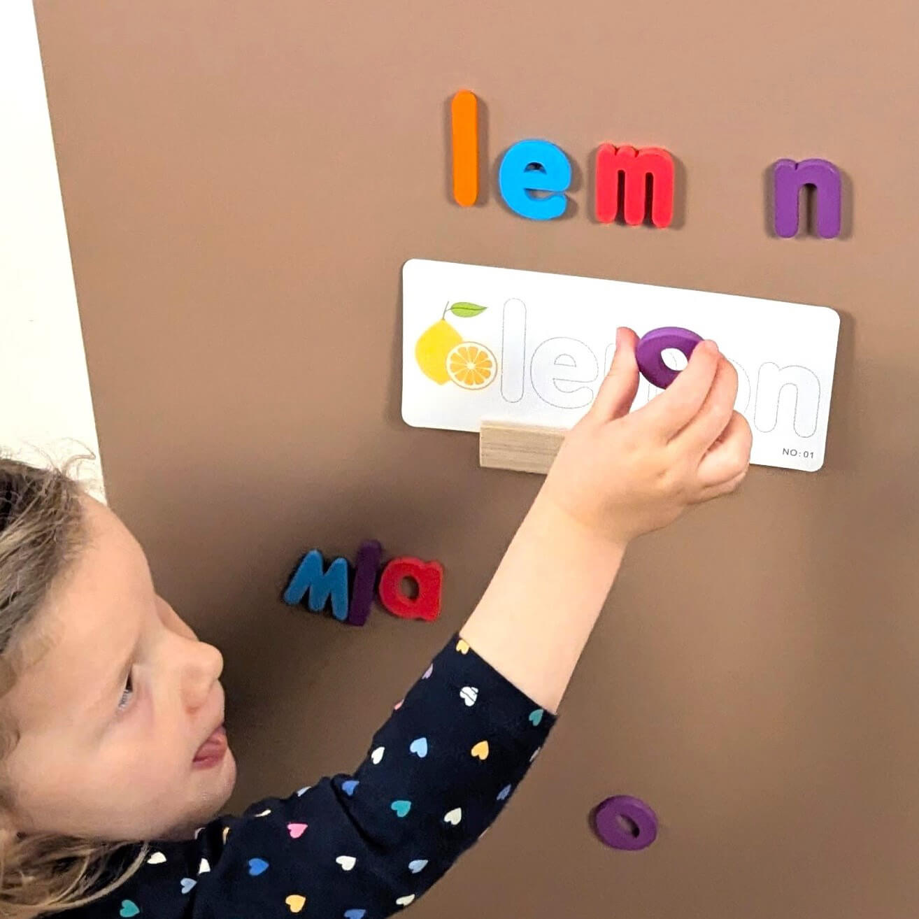 a child reaching to place a magnetic letter on a brown board