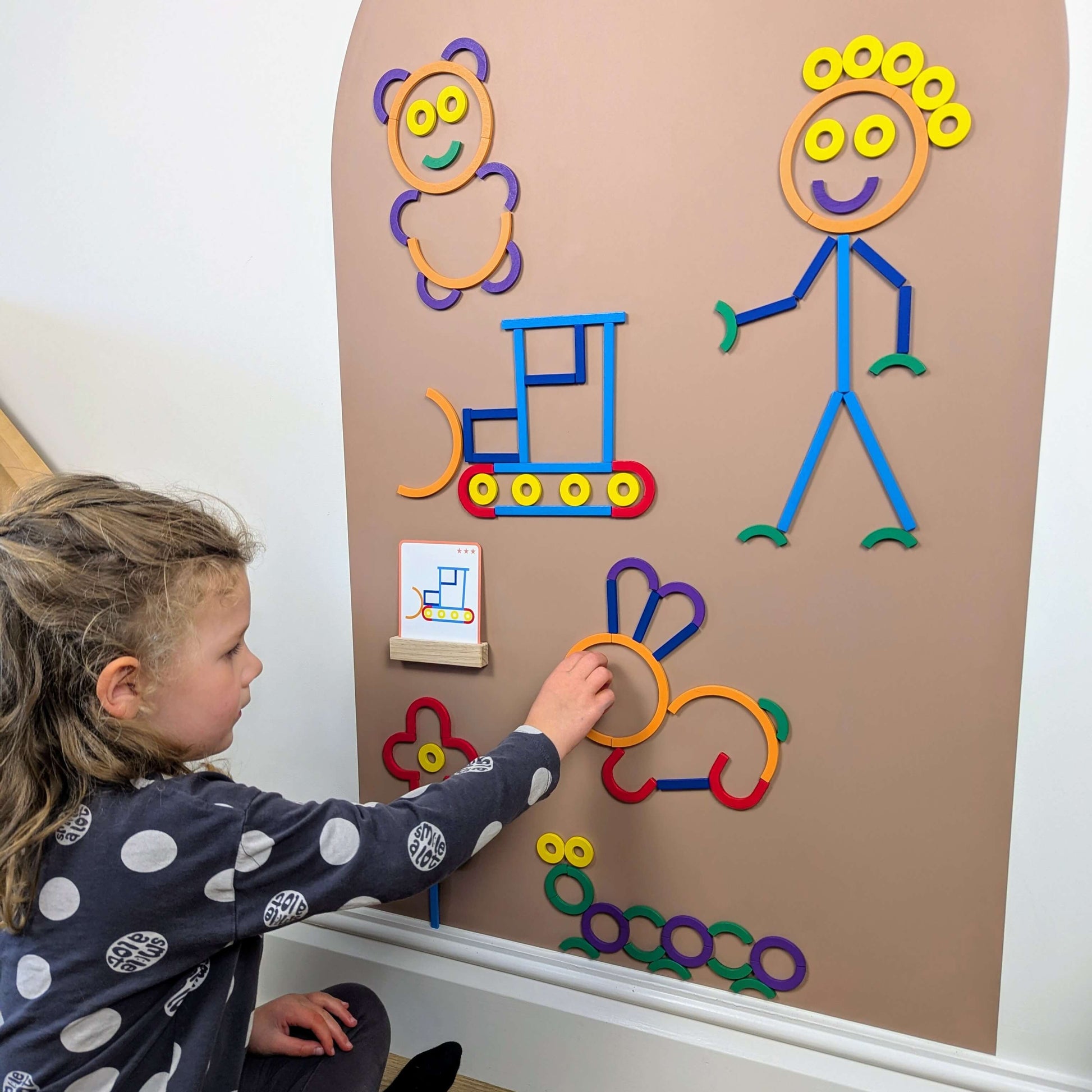 Child playing with a clay coloured wall decal with colourful wooden magnetic shapes