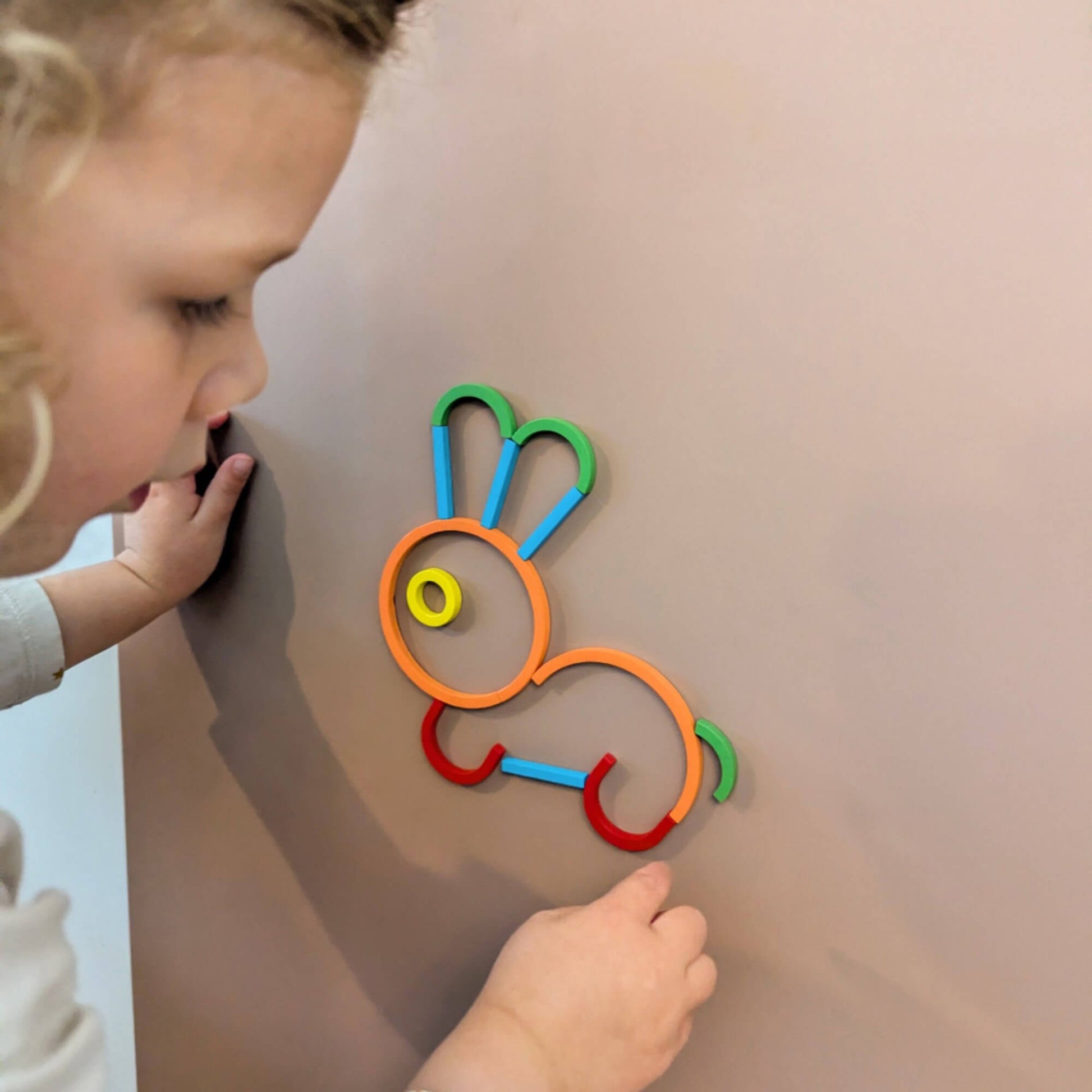 a child making the shape of a rabbit our of magnetic colourful wooden shapes on a clay coloured board