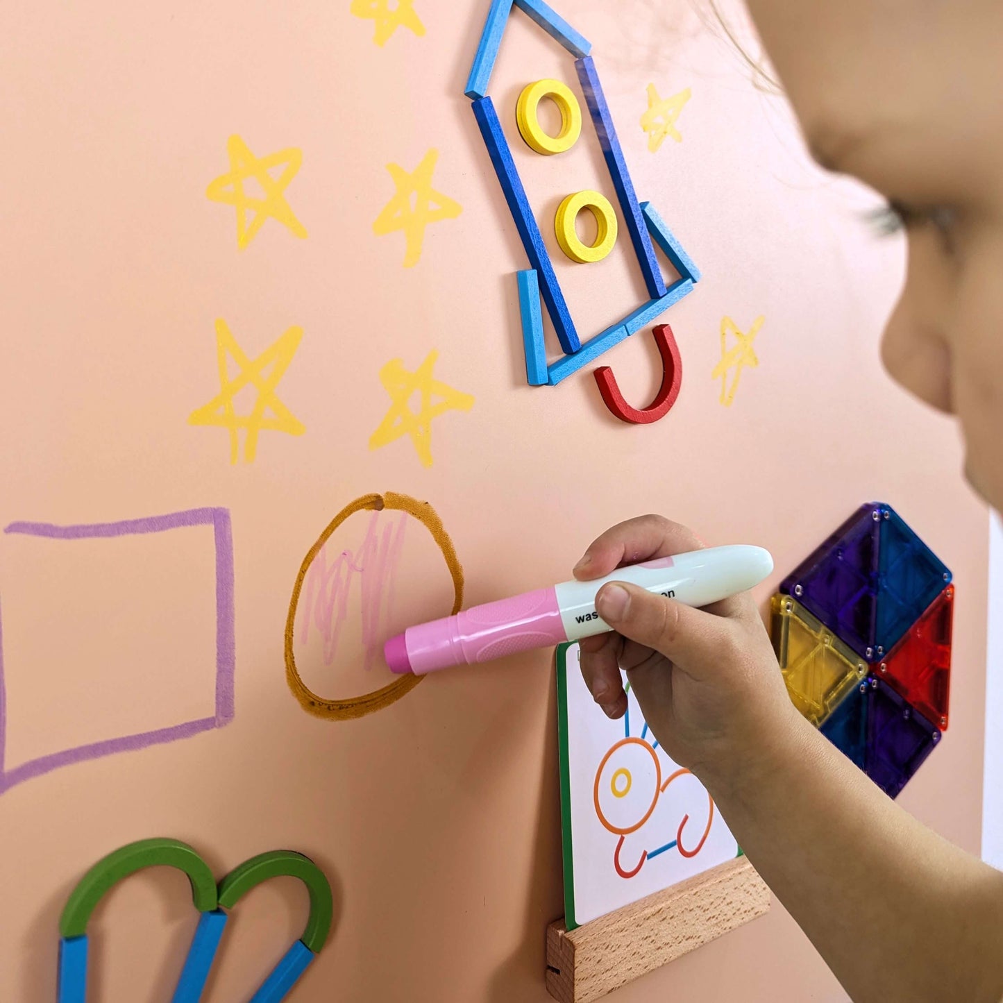 Closeup of child drawing with a pink crayon on a blush pink background