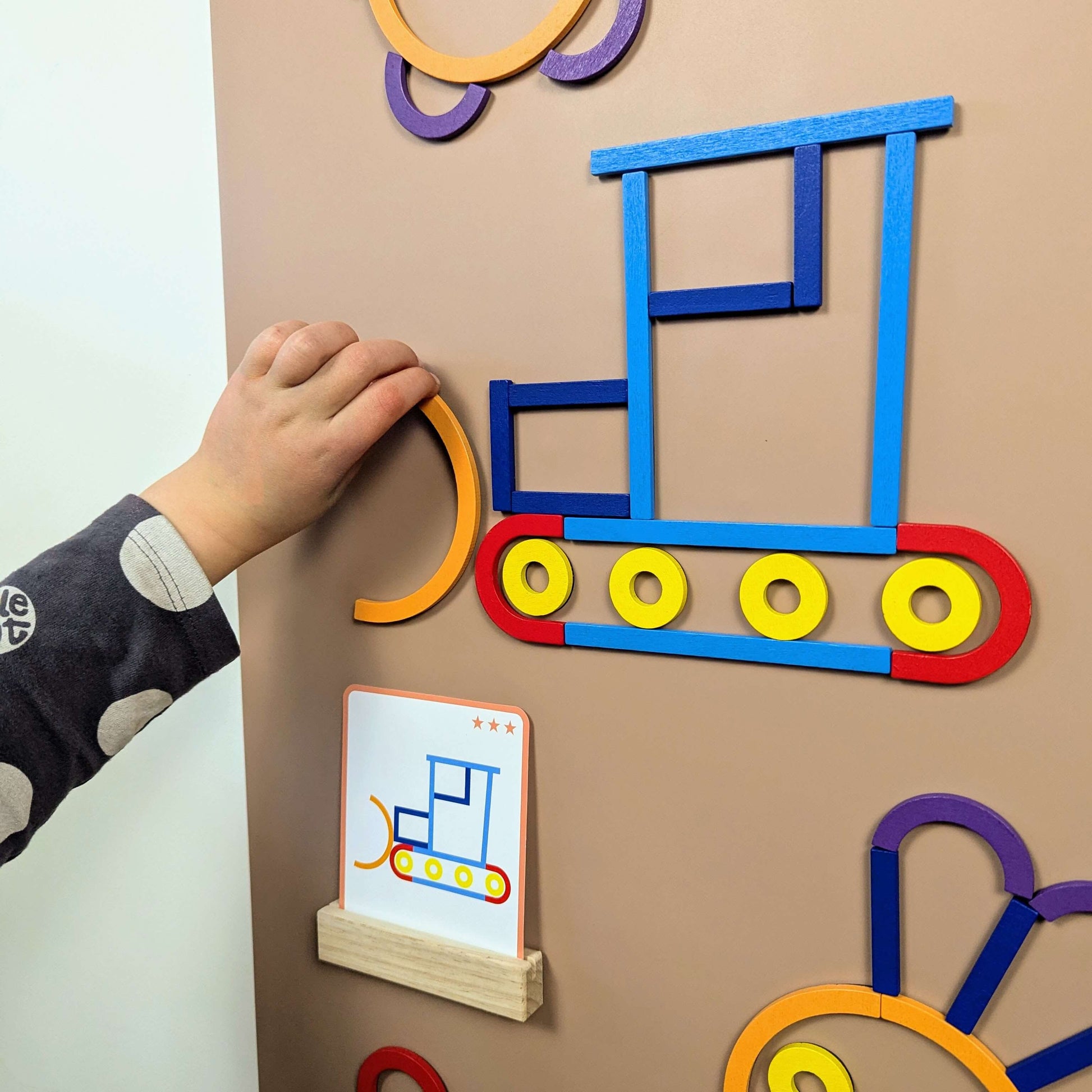 Close up of child playing with colourful wooden magnetic shapes on wall decal